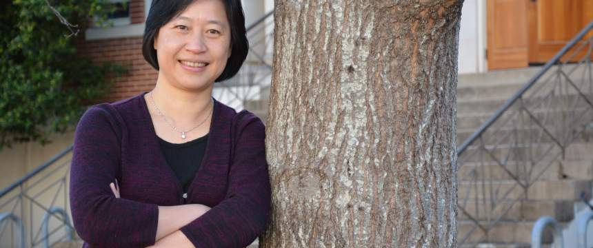 CJ Tsai stands with her arms crossed and her left shoulder leaning against a tree.